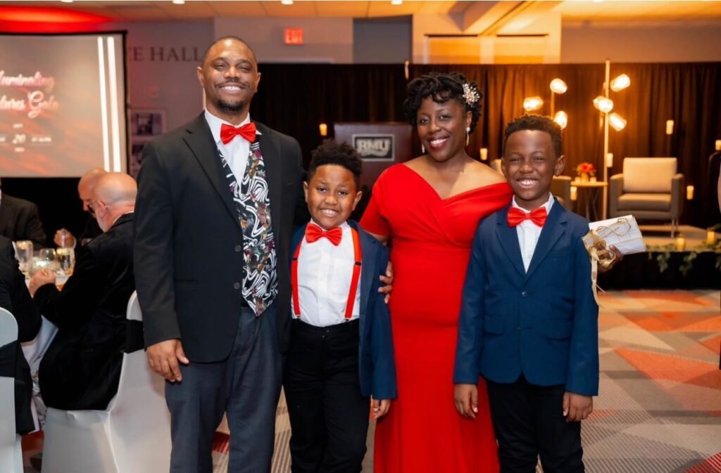 ACF Pittsburgh Chapter President, Dr. Eliada Wosu Griffin-EL smiling with her husband and two sons at a formal gala, all dressed in coordinated red and navy attire, standing together in a warmly lit banquet hall.